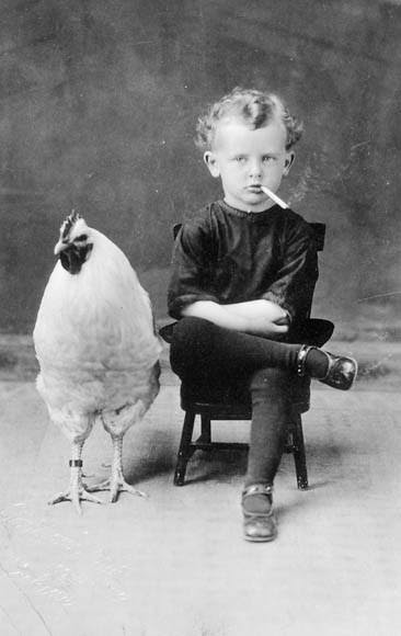 Kid smoking sitting next to a chicken.  